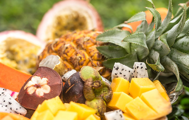 A bowl of mixed tropical fruits displayed on a bright green grassy area.