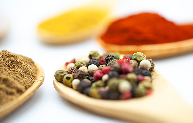 Wooden spoons filled with a variety of spices and herbs, highlighting their rich colors and natural textures.